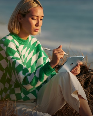 A person on the beach holding their Apple Pencil Pro in one hand and a blue iPad mini in the other